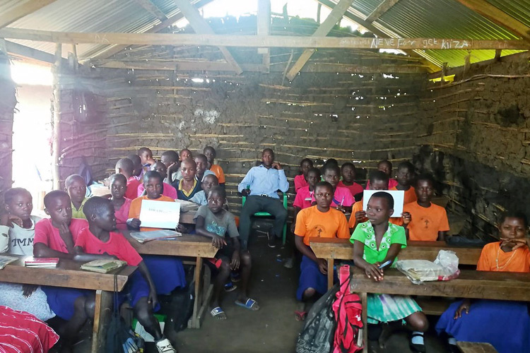 Ugandan children in a mud hut classroom with their teacher.